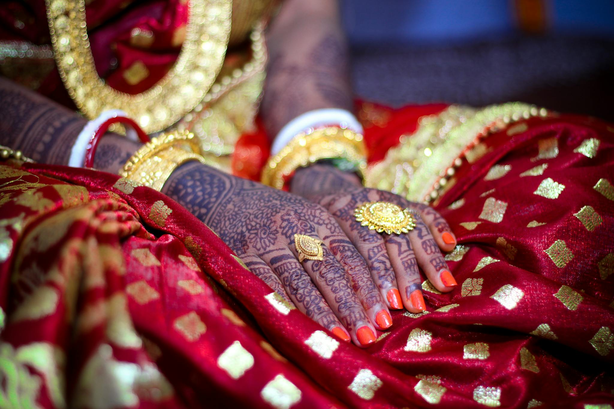 Close-up of a bride's henna-adorned hands in traditional attire, showcasing intricate designs.
