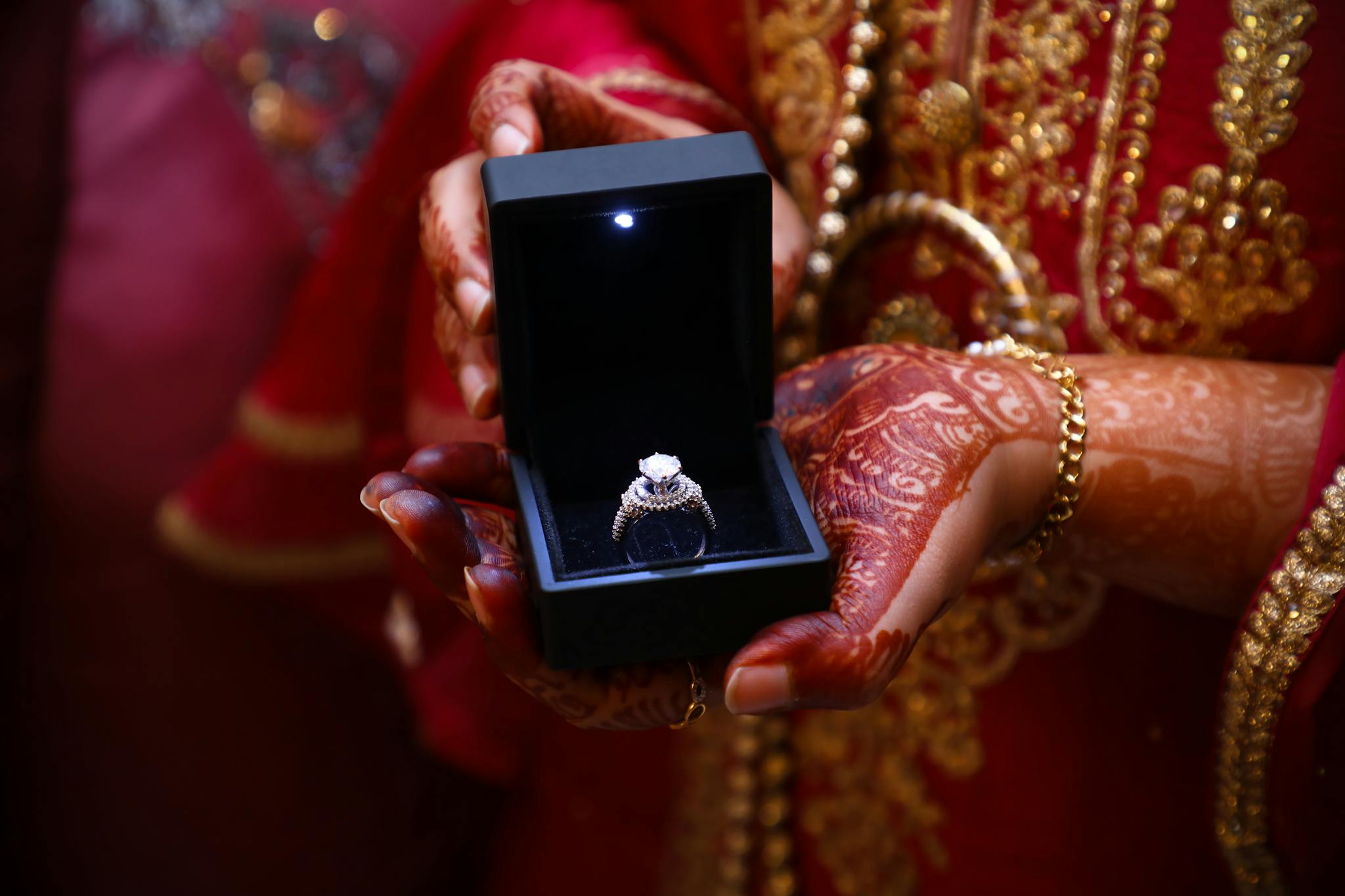 Elegant diamond ring in luxurious box held by hands with intricate henna designs.